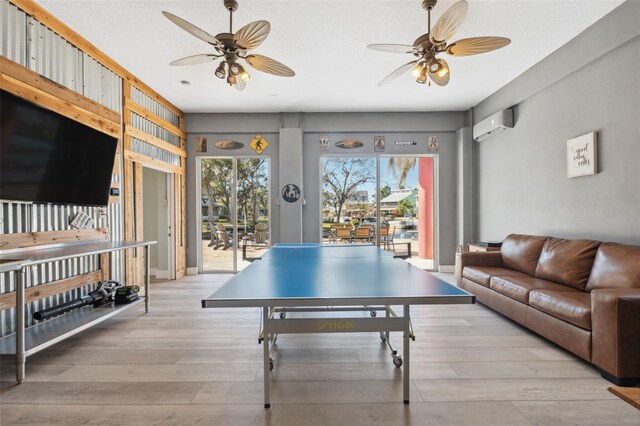 rec room with ceiling fan, a wall unit AC, and light wood-type flooring