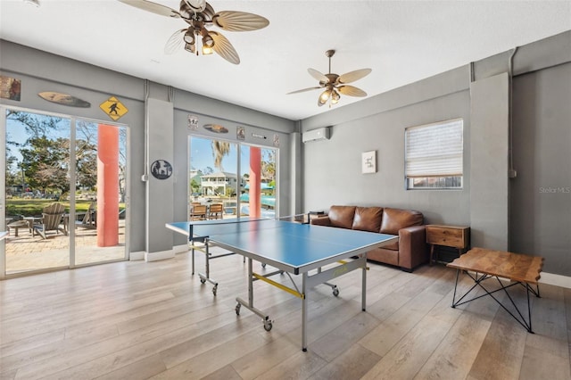 game room with ceiling fan, a wall unit AC, and light hardwood / wood-style flooring