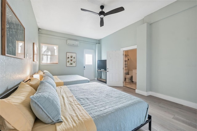 bedroom with ceiling fan, connected bathroom, a wall mounted AC, and light wood-type flooring