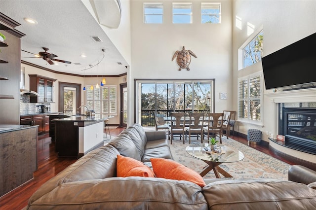 living room with sink, dark wood-type flooring, a premium fireplace, ceiling fan, and ornamental molding