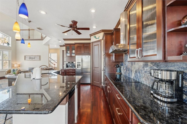 kitchen with dark wood-type flooring, wall chimney exhaust hood, decorative light fixtures, stainless steel fridge with ice dispenser, and dark stone countertops