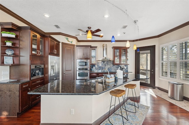 kitchen featuring sink, appliances with stainless steel finishes, a kitchen island with sink, hanging light fixtures, and wall chimney exhaust hood