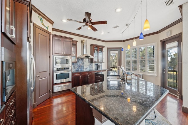 kitchen with wall chimney exhaust hood, sink, decorative light fixtures, appliances with stainless steel finishes, and a large island