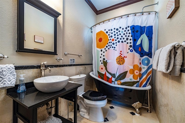 bathroom with tile patterned floors, toilet, sink, crown molding, and tile walls