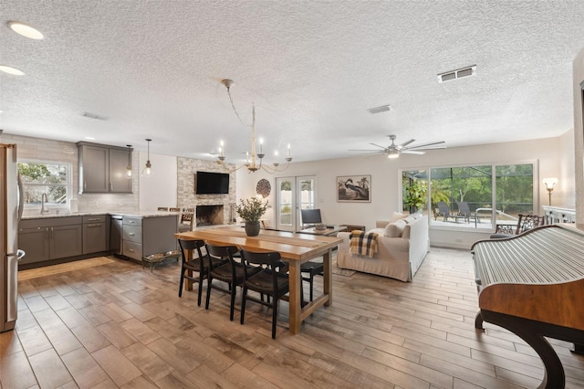 dining room with ceiling fan, a stone fireplace, dark wood-type flooring, and a textured ceiling