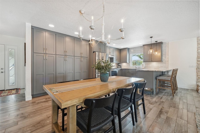 kitchen with decorative light fixtures, stainless steel refrigerator, gray cabinets, light stone countertops, and light hardwood / wood-style floors