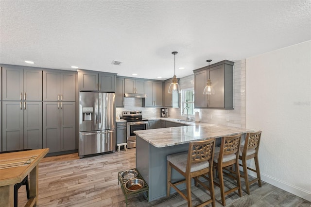 kitchen featuring gray cabinets, appliances with stainless steel finishes, light hardwood / wood-style floors, decorative light fixtures, and kitchen peninsula