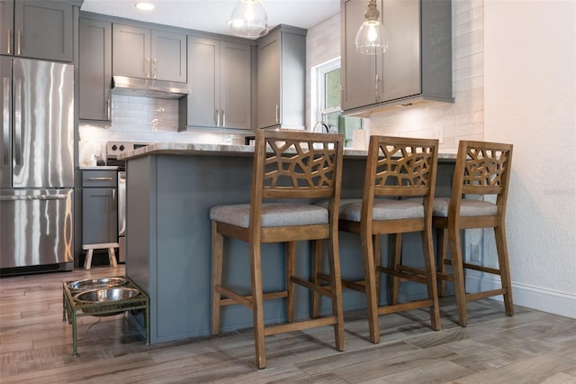 kitchen with gray cabinets, a breakfast bar, stainless steel refrigerator, tasteful backsplash, and light hardwood / wood-style flooring