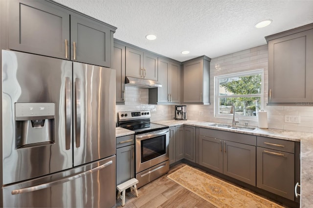 kitchen with sink, gray cabinetry, stainless steel appliances, light stone countertops, and light wood-type flooring