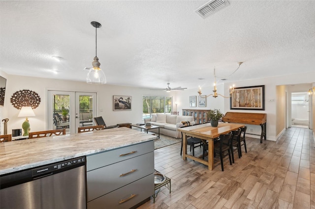 kitchen with light stone counters, hanging light fixtures, light wood-type flooring, dishwasher, and a healthy amount of sunlight