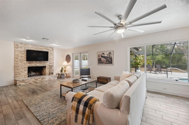 living room with a stone fireplace, light hardwood / wood-style floors, ceiling fan, and a textured ceiling