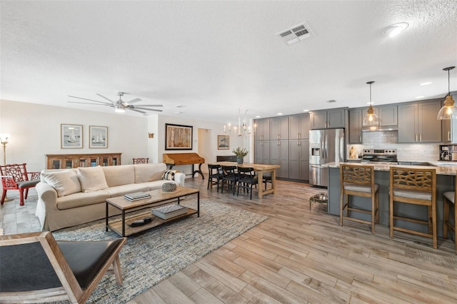 living room featuring ceiling fan with notable chandelier, a textured ceiling, and light hardwood / wood-style floors