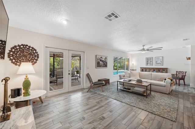 living room featuring french doors, ceiling fan, light hardwood / wood-style flooring, and a textured ceiling