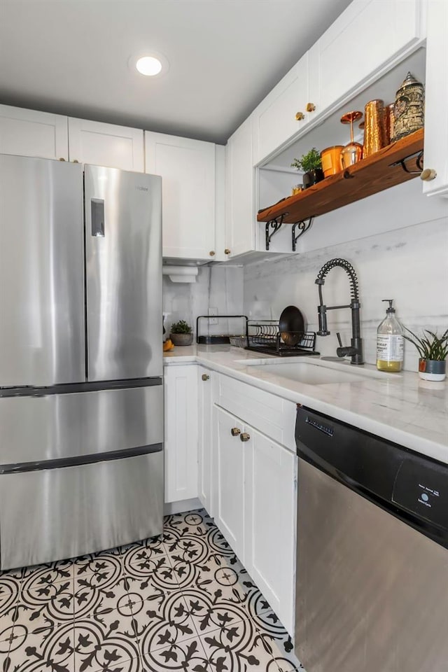 kitchen with appliances with stainless steel finishes, white cabinetry, sink, backsplash, and light stone counters