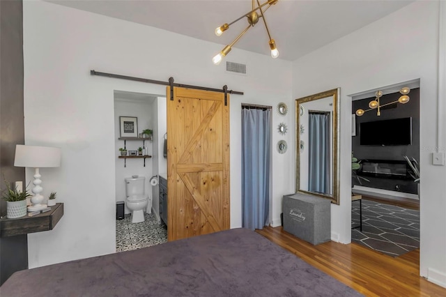 bedroom with ensuite bathroom, a barn door, and hardwood / wood-style floors