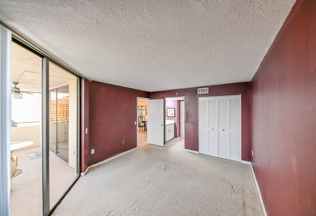 unfurnished bedroom featuring light colored carpet, access to exterior, a textured ceiling, and a closet