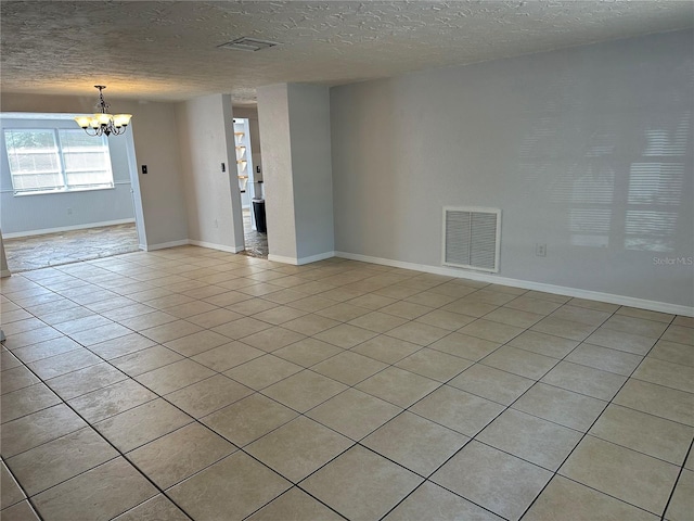 tiled empty room with a textured ceiling and an inviting chandelier