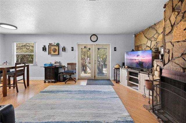 living room featuring french doors, a fireplace, a textured ceiling, and light hardwood / wood-style flooring