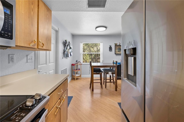 kitchen with light hardwood / wood-style flooring, a textured ceiling, and appliances with stainless steel finishes