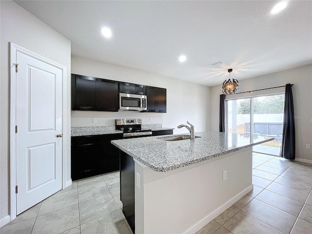 kitchen featuring pendant lighting, sink, appliances with stainless steel finishes, a kitchen island with sink, and light stone counters