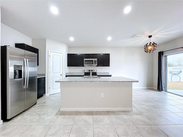 kitchen with light stone counters, decorative light fixtures, stainless steel appliances, and a center island with sink