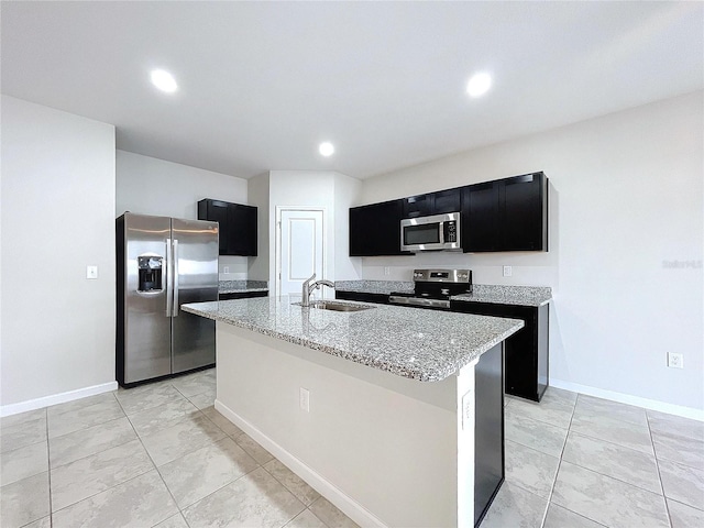 kitchen featuring appliances with stainless steel finishes, sink, light stone countertops, and a kitchen island with sink