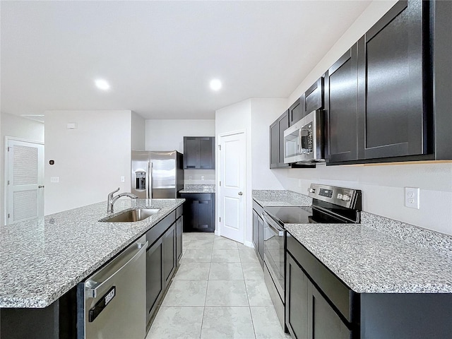 kitchen with sink, light stone counters, light tile patterned floors, stainless steel appliances, and a kitchen island with sink