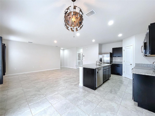 kitchen with an island with sink, appliances with stainless steel finishes, sink, and light stone counters