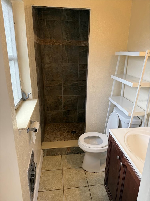 bathroom with tiled shower, vanity, toilet, and tile patterned flooring