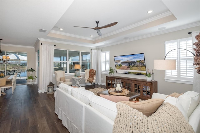 living room with dark wood-type flooring, ornamental molding, a tray ceiling, and ceiling fan with notable chandelier