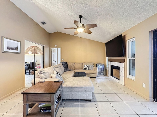 living room featuring light tile patterned floors, lofted ceiling, visible vents, a tiled fireplace, and a ceiling fan