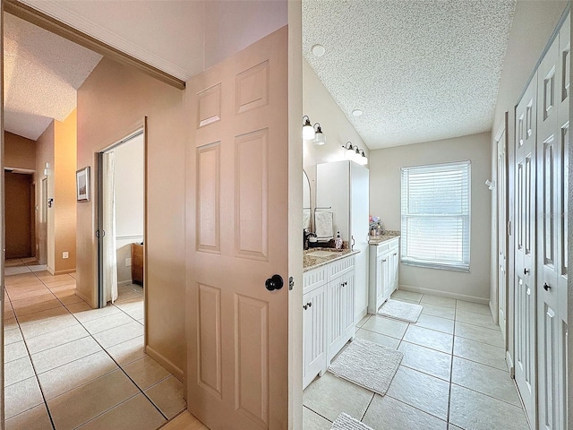 bathroom with tile patterned flooring, vanity, baseboards, and a textured ceiling