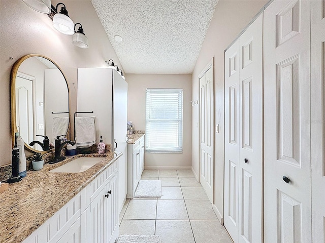 bathroom with baseboards, two vanities, tile patterned floors, a textured ceiling, and a sink