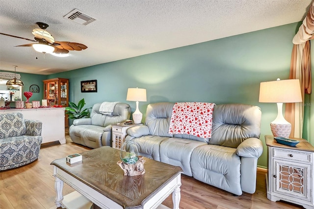 living room featuring ceiling fan, light hardwood / wood-style flooring, and a textured ceiling