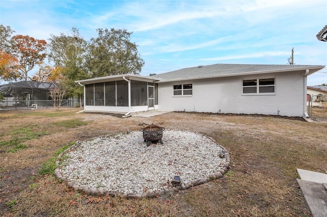 rear view of house featuring an outdoor fire pit, a yard, and a sunroom