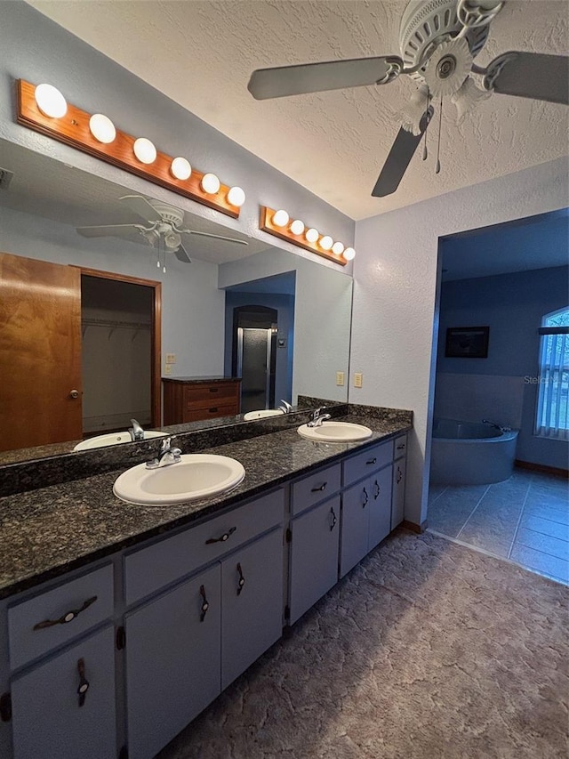 bathroom with ceiling fan, tile patterned flooring, a bathtub, vanity, and a textured ceiling