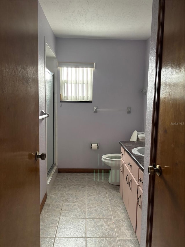 bathroom featuring toilet, a textured ceiling, vanity, a shower with door, and tile patterned flooring