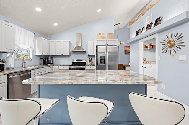 kitchen with wall chimney range hood, washer and clothes dryer, appliances with stainless steel finishes, a center island, and decorative light fixtures