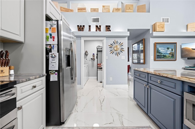 kitchen featuring blue cabinets, white cabinetry, appliances with stainless steel finishes, and washing machine and clothes dryer