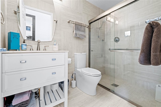 bathroom featuring vanity, toilet, a shower with door, and tile walls