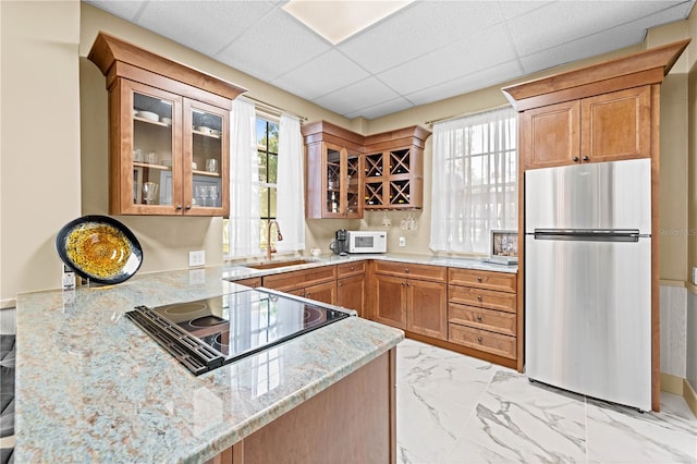 kitchen featuring sink, stainless steel fridge, black electric stovetop, light stone countertops, and kitchen peninsula