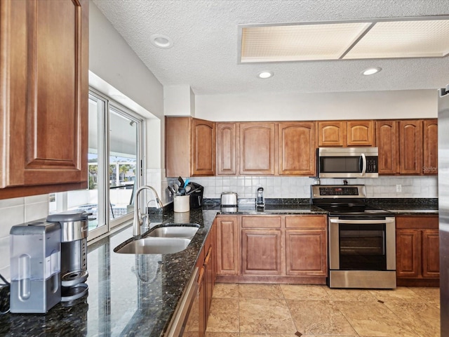 kitchen with stainless steel appliances, sink, backsplash, and dark stone counters