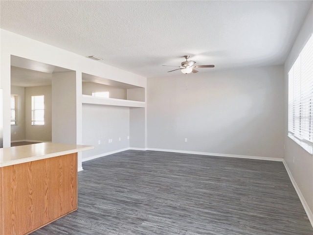 interior space with a healthy amount of sunlight, ceiling fan, dark wood-type flooring, and a textured ceiling