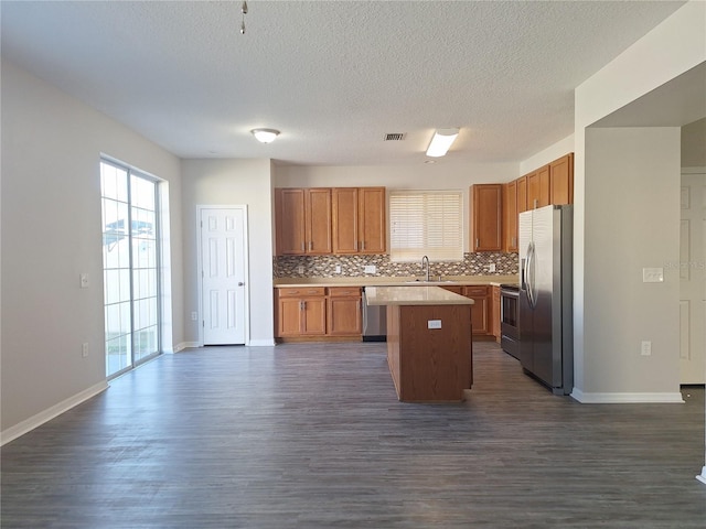 kitchen featuring appliances with stainless steel finishes, tasteful backsplash, sink, dark hardwood / wood-style flooring, and a center island