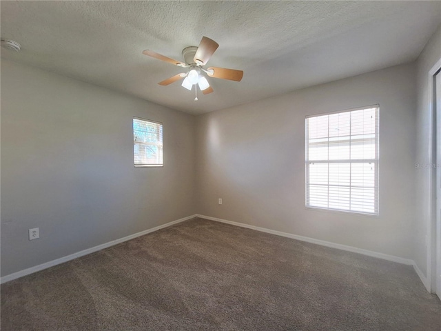 empty room with ceiling fan, a textured ceiling, a healthy amount of sunlight, and dark colored carpet