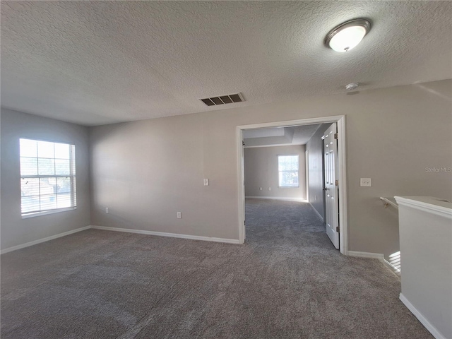 unfurnished room featuring dark carpet, a textured ceiling, and a wealth of natural light