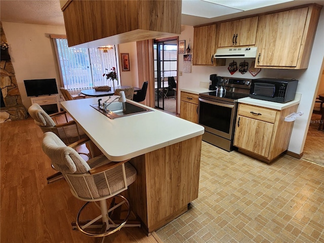 kitchen featuring a breakfast bar, sink, a textured ceiling, light wood-type flooring, and electric stove