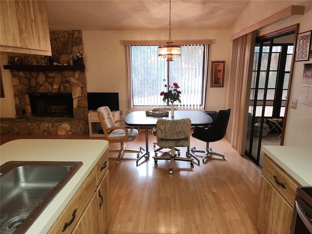 dining space featuring sink, a stone fireplace, light hardwood / wood-style floors, and a textured ceiling