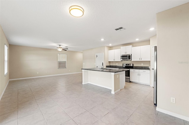 kitchen featuring ceiling fan, appliances with stainless steel finishes, a center island with sink, white cabinets, and a kitchen bar