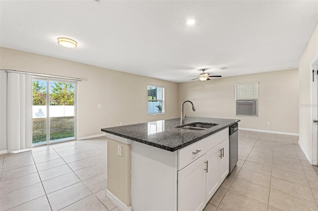 kitchen with sink, a kitchen island with sink, white cabinets, stainless steel dishwasher, and dark stone counters